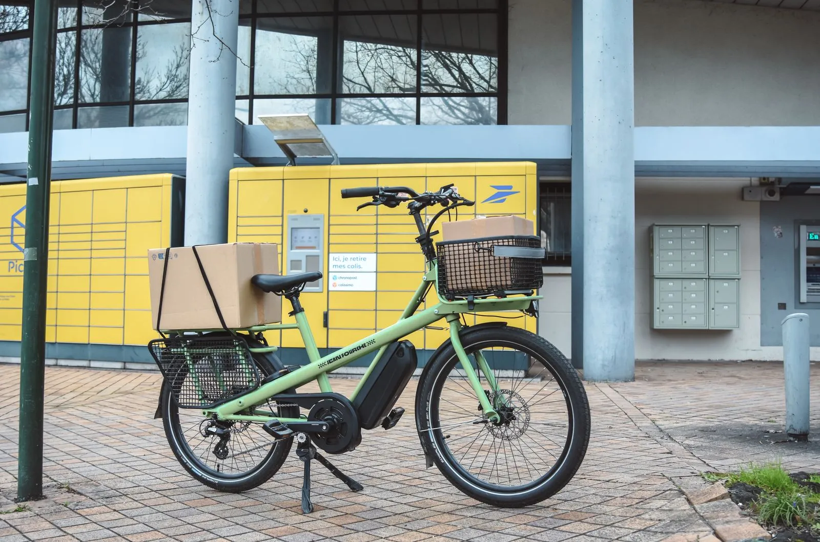 Green electric cargo bike with parcels at La Poste in France, showcasing urban delivery solutions.